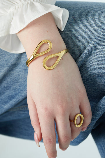 Bracciale rigido dorato a goccia **minimal**in acciaio inossidabile, indossato al polso in abbinamento con finitura lucida.